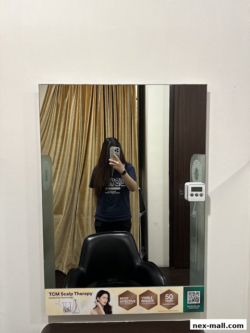 A person takes a mirror selfie in a hair salon, showing a chair and promotional material.
