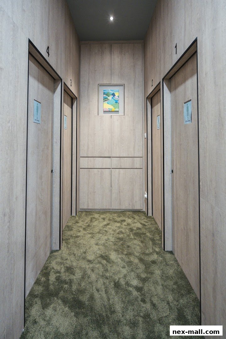 A hallway with numbered doors and a plush green carpet leading to a framed artwork.