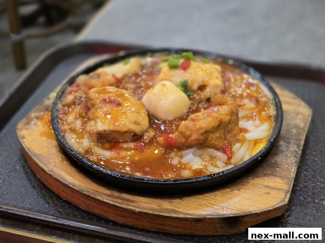A sizzling hot plate dish with tofu, sauce, and noodles, served on a wooden base.