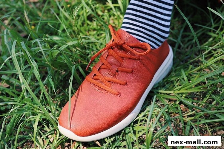 A close-up shot of a person wearing a stylish orange sneaker with striped socks, standing on grass.