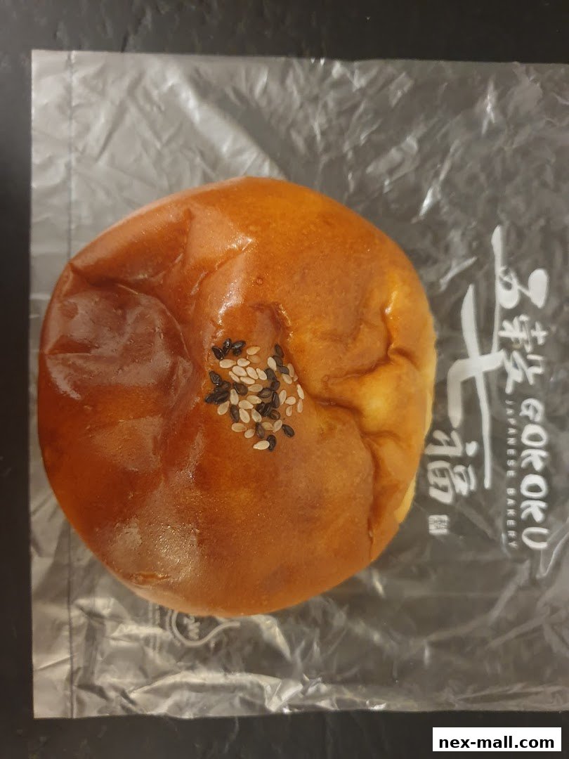 A golden-brown Japanese sweet bun topped with sesame seeds, packaged in plastic.