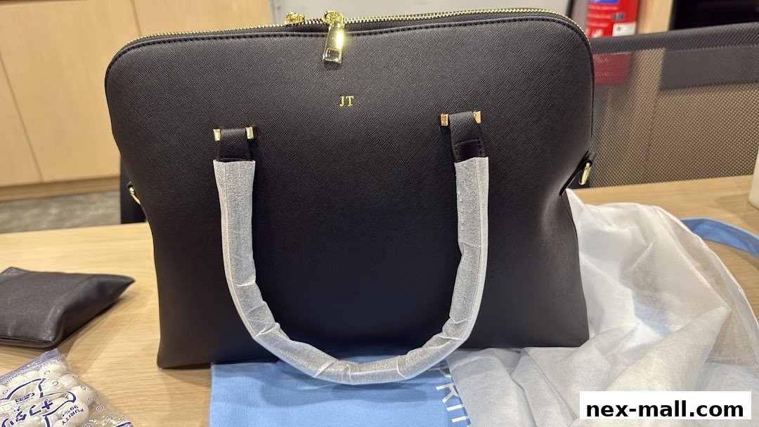 A black personalized tote bag with gold initials 'JT' and protective plastic on the handles.