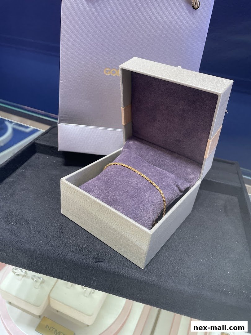 A gold bracelet displayed in an open jewelry box with a shopping bag in the background.
