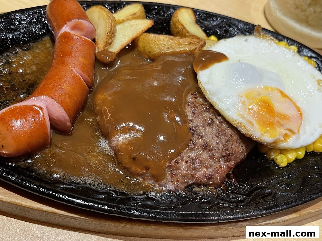 A sizzling hot plate meal featuring a sausage, hamburger steak, fried egg, and potato wedges.
