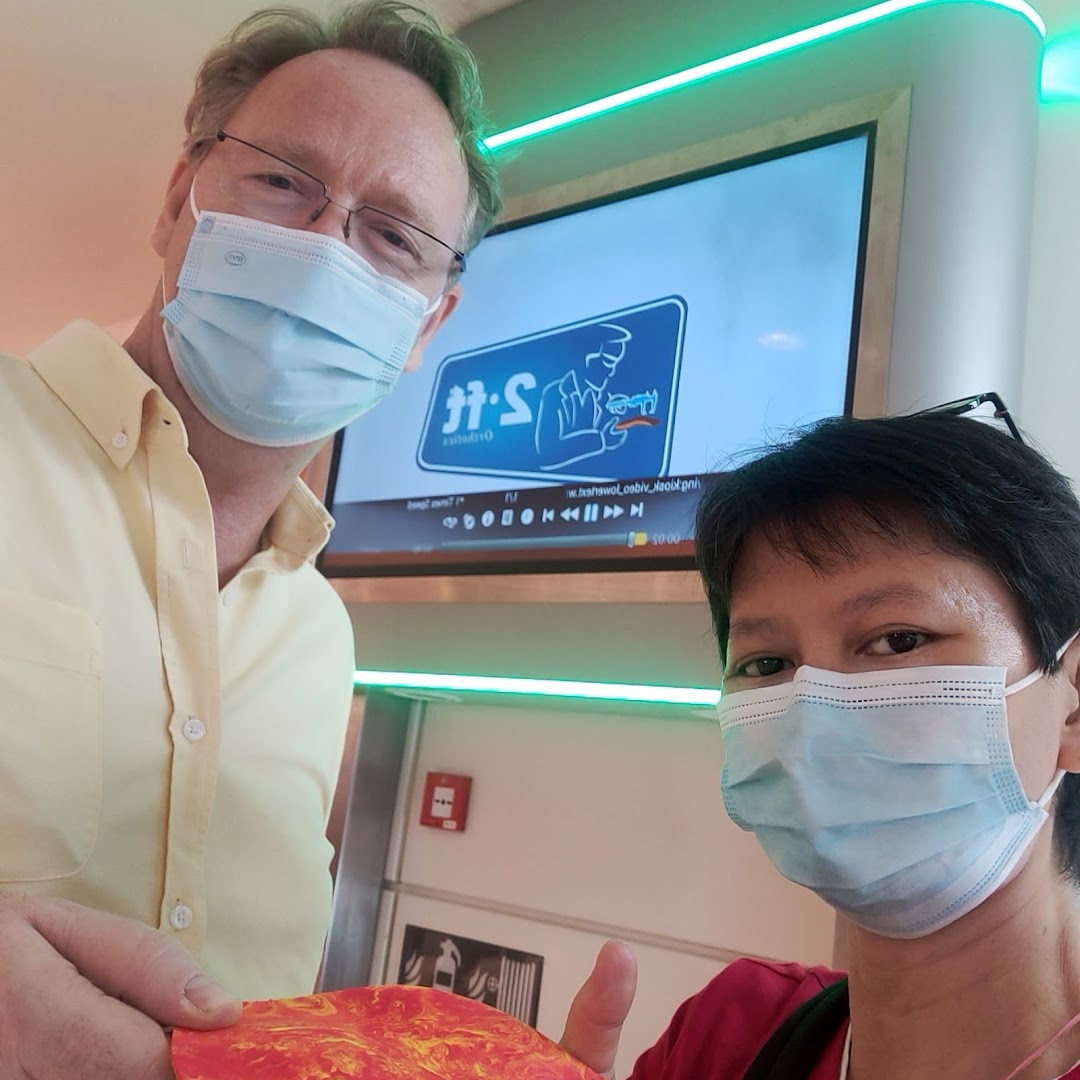 Two masked individuals inside 2ft Orthotics, with the brand's logo visible on a screen.