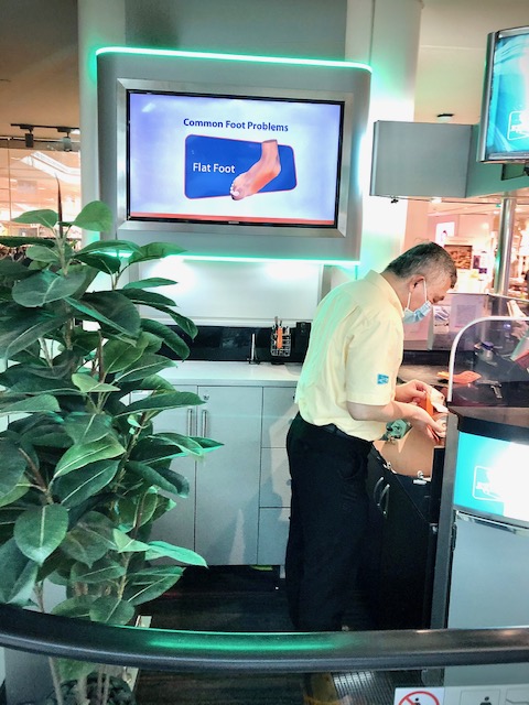 An employee at 2ft Orthotics works at a counter with a screen displaying foot health information.