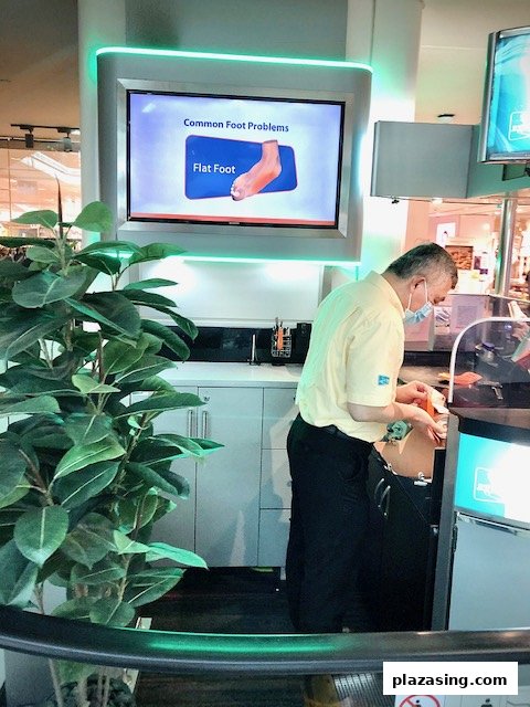 An employee at 2ft Orthotics works at a counter with a screen displaying foot health information.