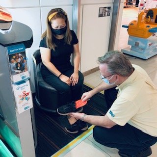 A staff member assists a customer with footwear, demonstrating orthotic solutions.