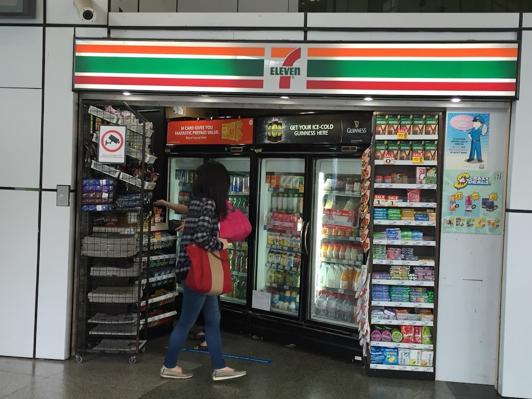 The entrance of a 7-Eleven convenience store with a customer browsing chilled drinks and snacks.
