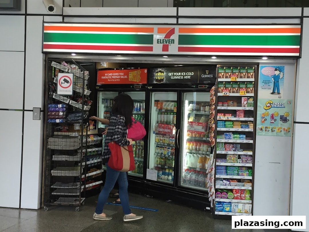 The entrance of a 7-Eleven convenience store with a customer browsing chilled drinks and snacks.