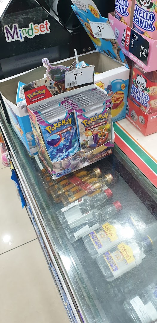 A retail counter display at 7-Eleven featuring Pokémon cards, popular snacks, and miniature alcohol bottles.