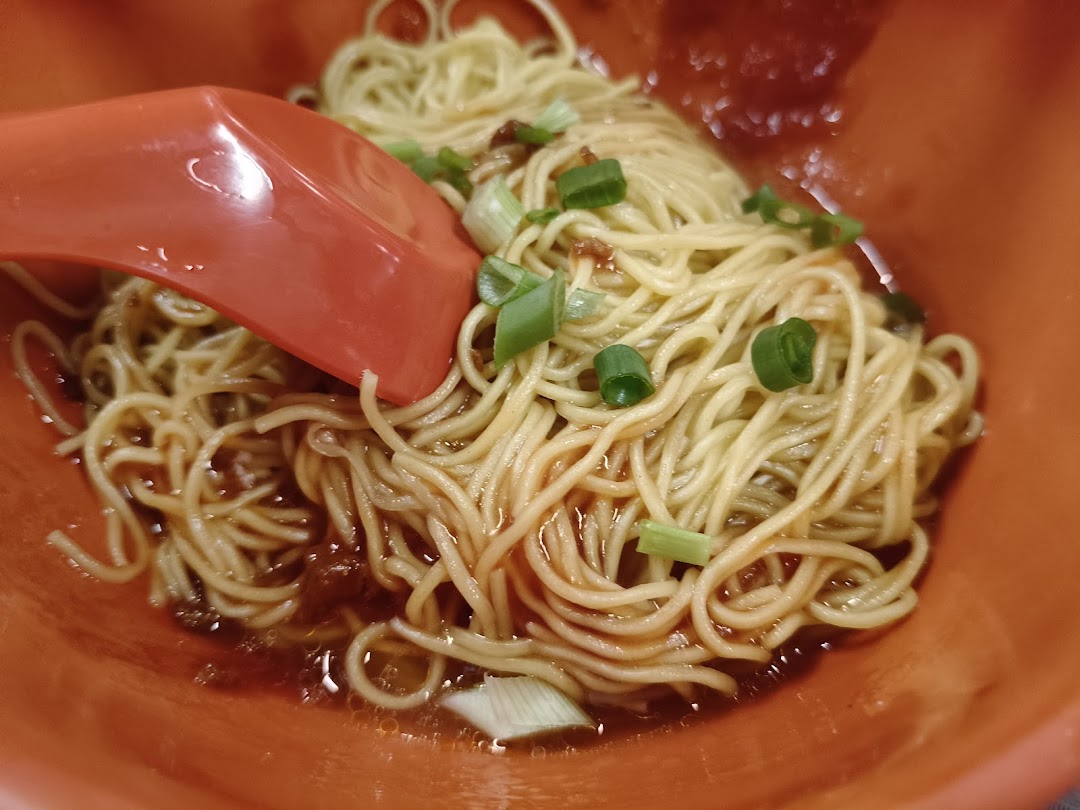 A close-up of delicious Teochew-style noodles with sauce and spring onions in an orange bowl.