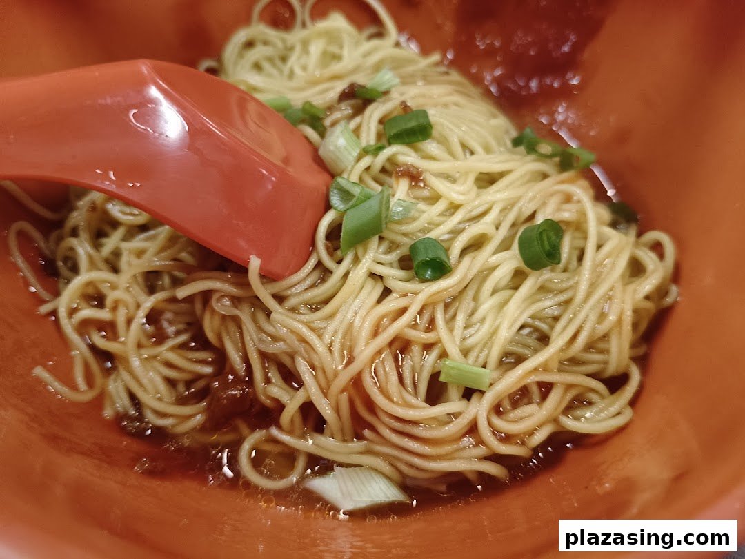 A close-up of delicious Teochew-style noodles with sauce and spring onions in an orange bowl.