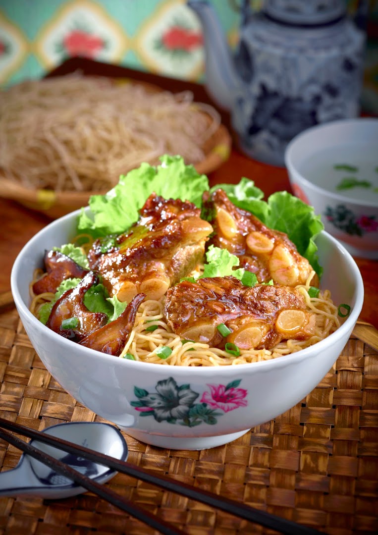 A close-up of a delicious bowl of noodles topped with braised pork ribs and fresh lettuce.