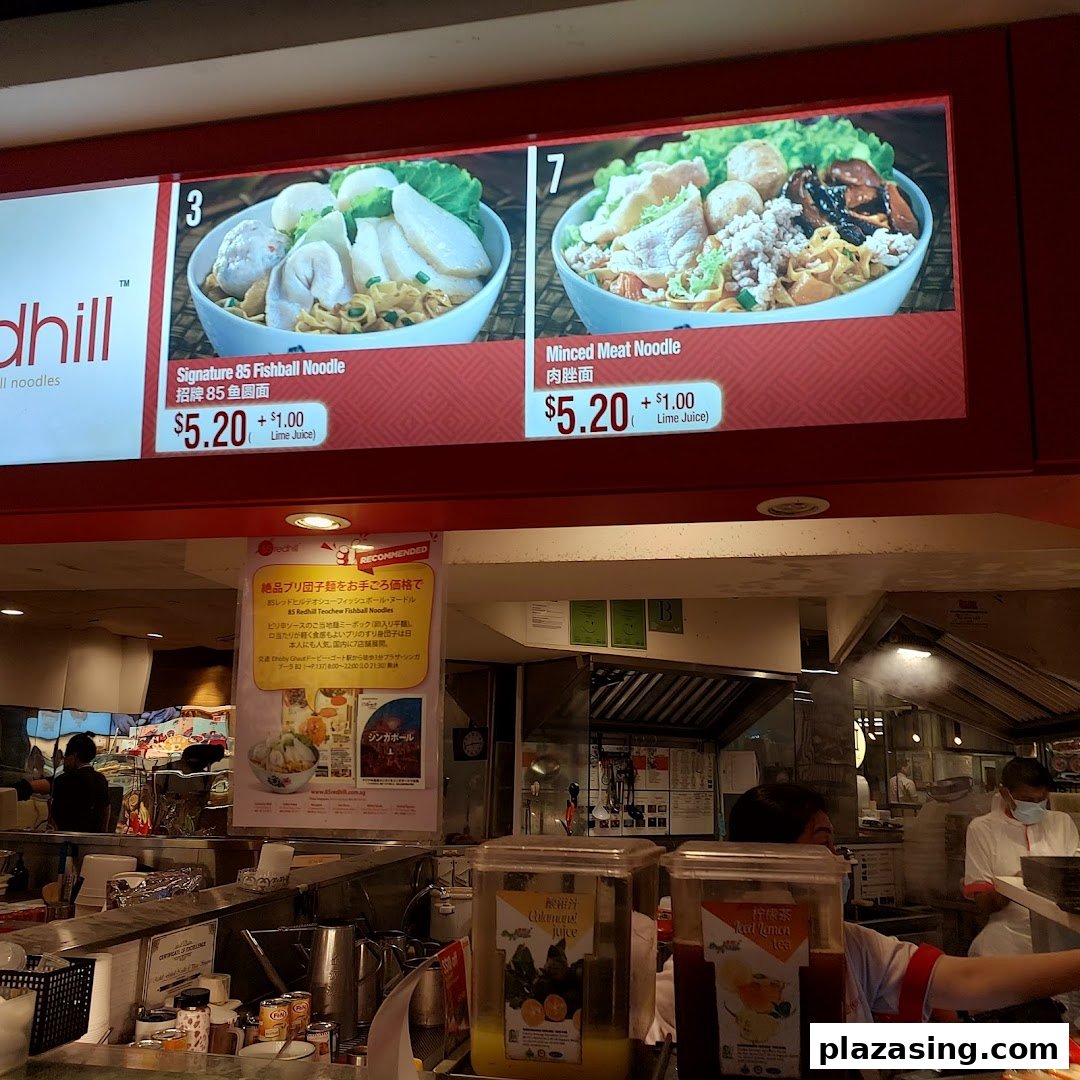 A digital menu board displays Signature Fishball Noodle and Minced Meat Noodle prices at a food stall.