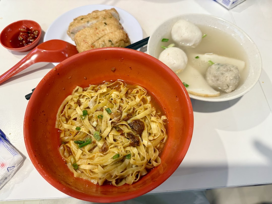 A delicious bowl of Teochew fishball noodles with soup, fishballs, and fishcake on a white table.