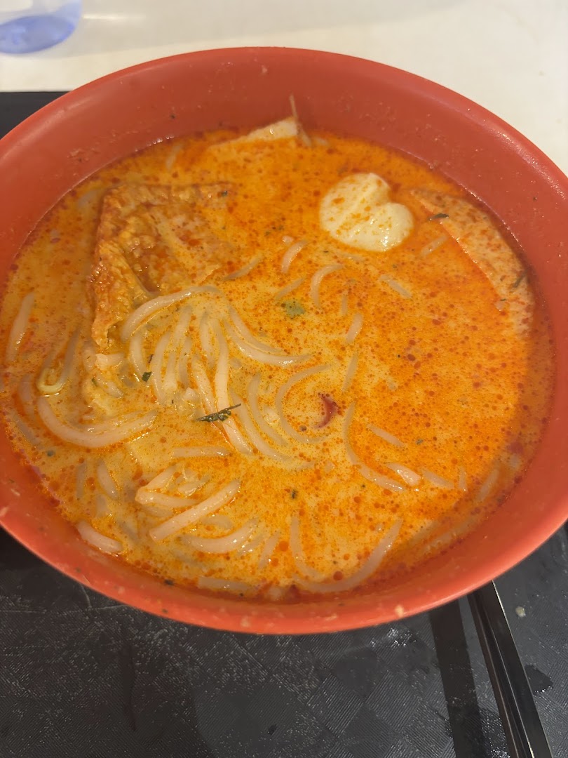 A vibrant bowl of laksa-style noodles with fishball and bean curd skin in a rich, spicy broth.