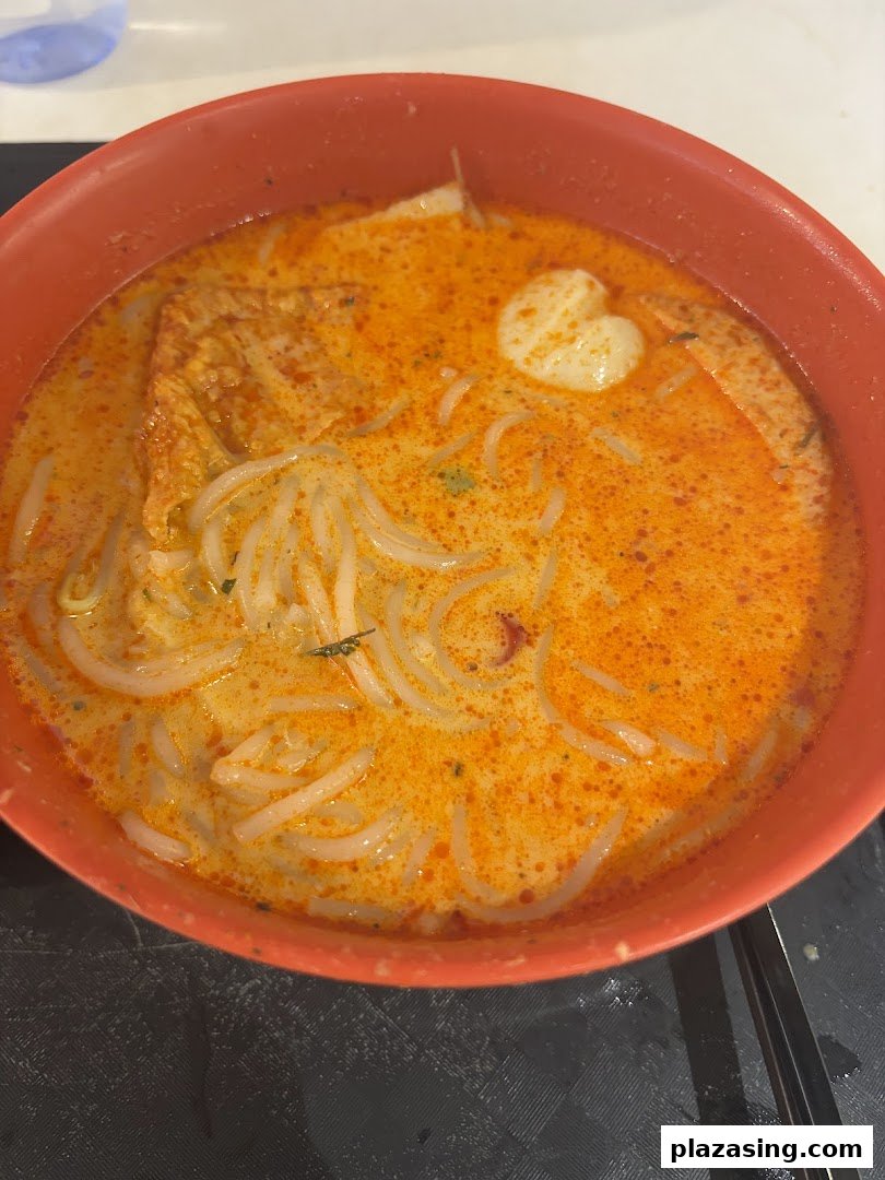 A vibrant bowl of laksa-style noodles with fishball and bean curd skin in a rich, spicy broth.