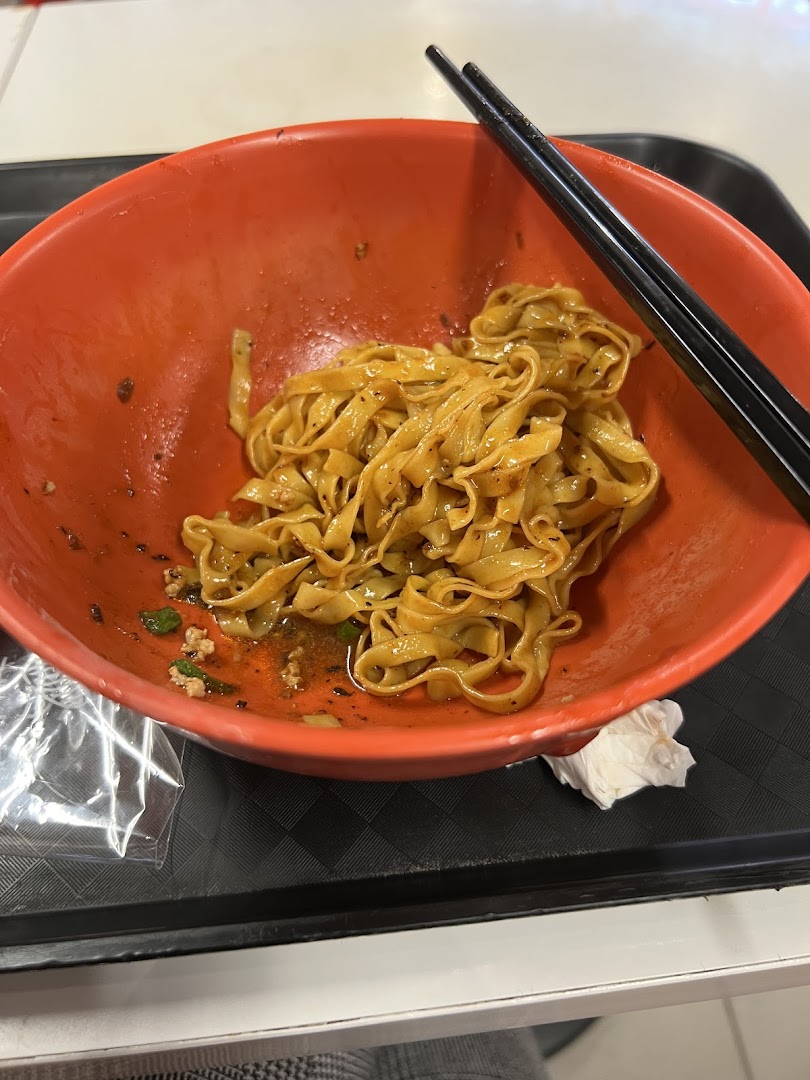 A vibrant orange bowl holds delicious Teochew fishball noodles with chopsticks, ready to be enjoyed.