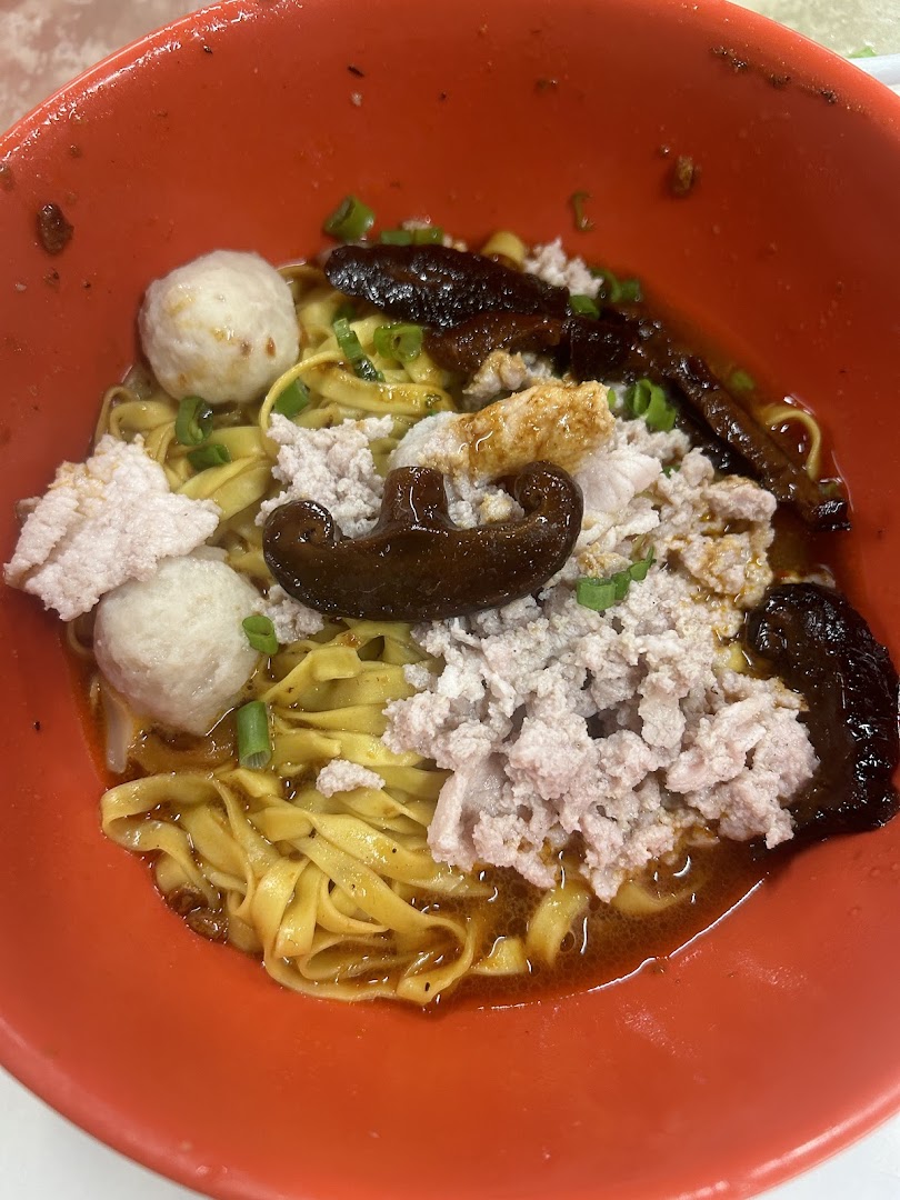 A close-up of a vibrant bowl of Teochew fishball noodles with minced pork, fishballs, and mushrooms.