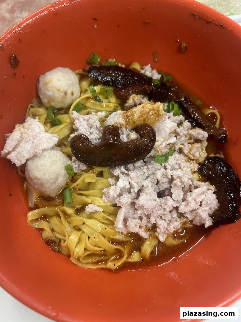 A close-up of a vibrant bowl of Teochew fishball noodles with minced pork, fishballs, and mushrooms.