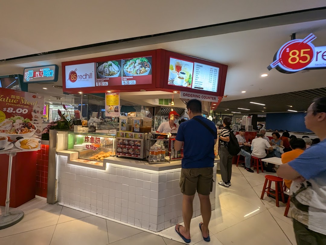 A bustling food stall featuring overhead menu boards displaying various noodle dishes and beverages.