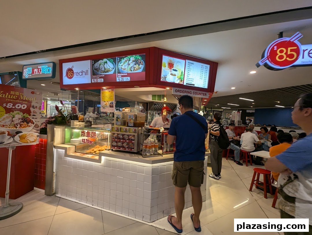 A bustling food stall featuring overhead menu boards displaying various noodle dishes and beverages.