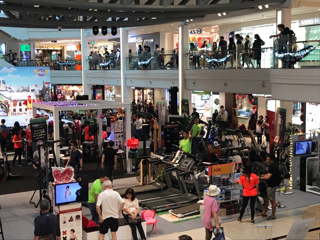 Busy mall interior showcasing Aibi's extensive fitness equipment display with many shoppers browsing.