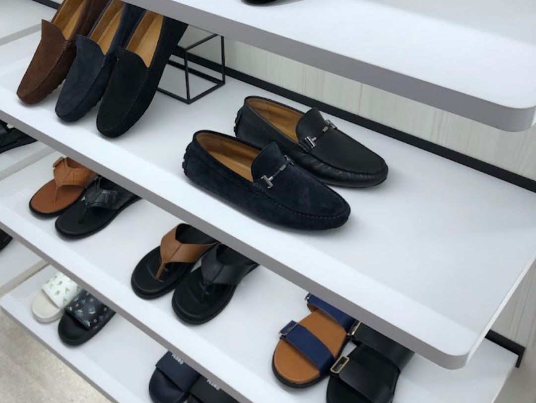 A retail display showcasing various men's shoes, including loafers and sandals, on white shelves.