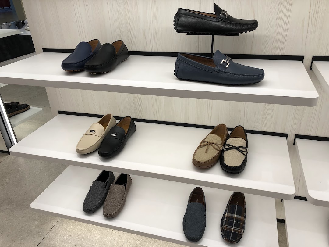 A display of various stylish men's loafers and driving shoes on white shelves inside the ALDO store.