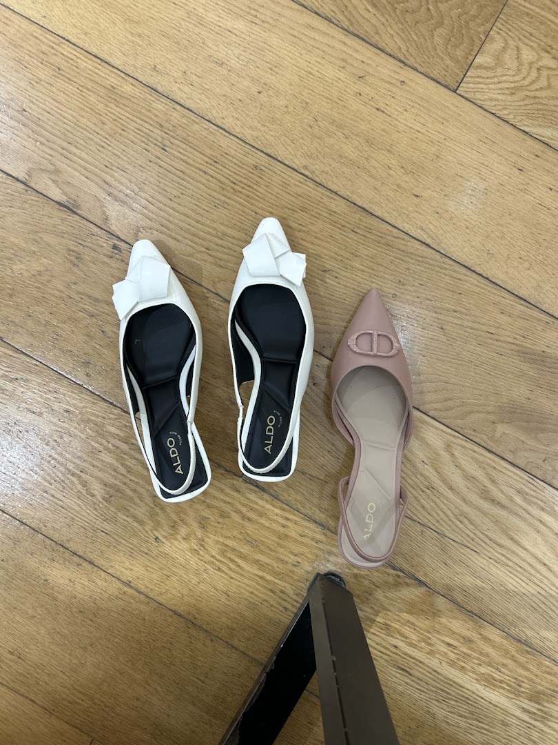 Three pairs of stylish ALDO shoes, two white and one nude, displayed on a wooden floor.