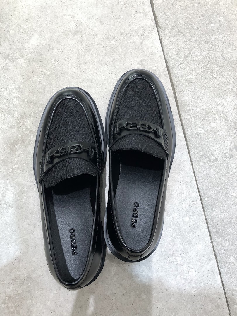 A pair of black Pedro brand loafers with textured uppers and metal detailing on a light floor.