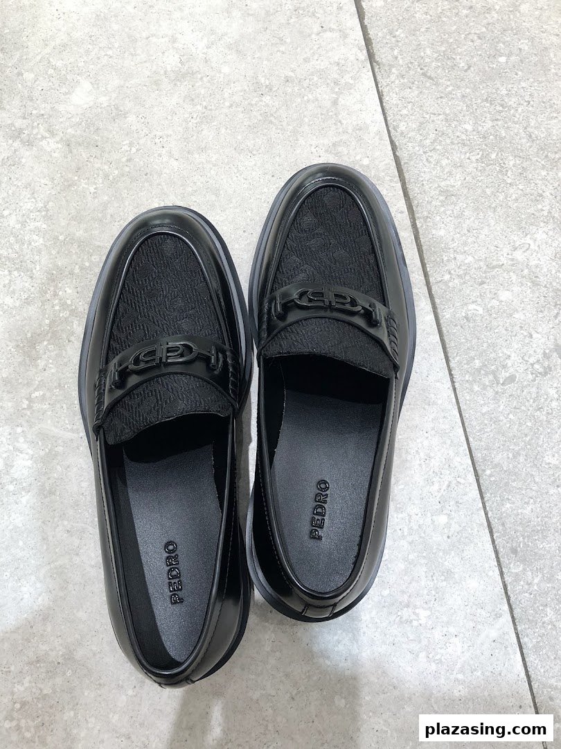 A pair of black Pedro brand loafers with textured uppers and metal detailing on a light floor.