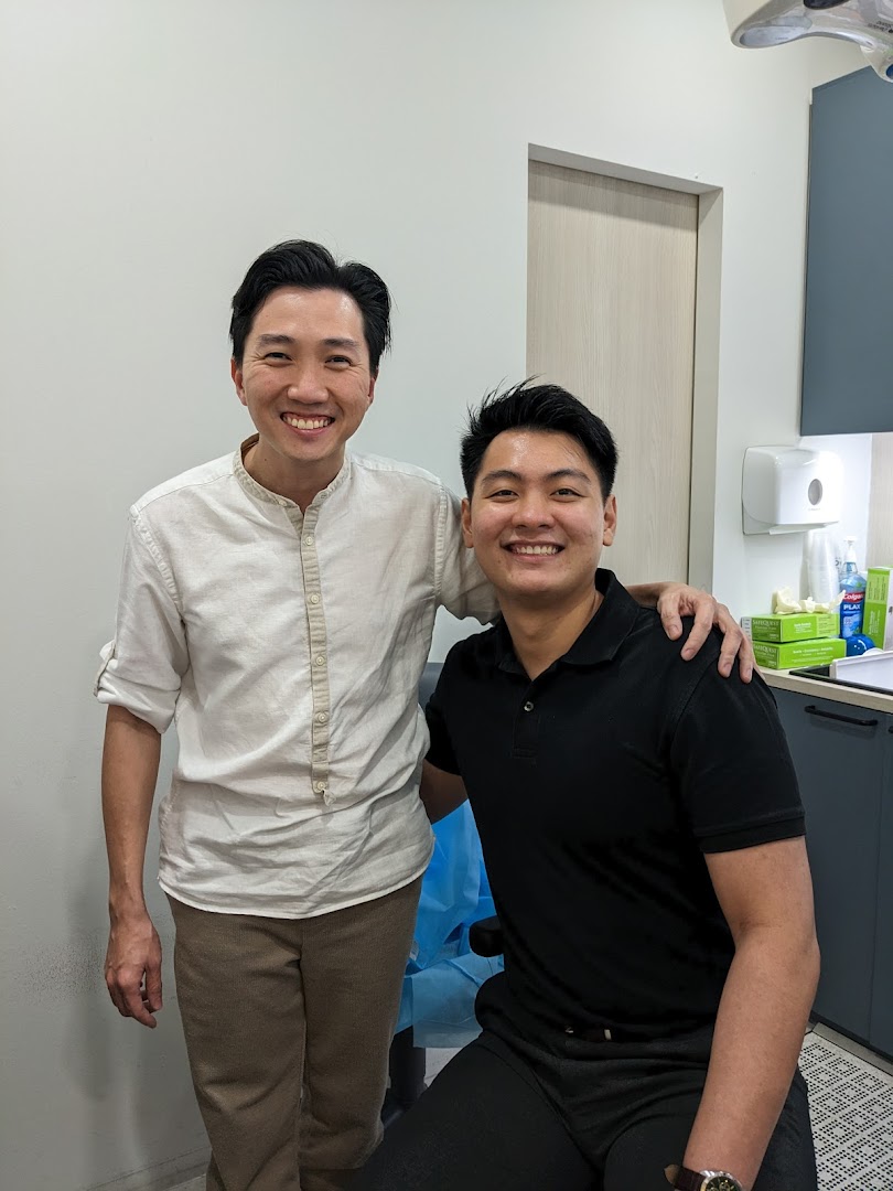 Two smiling men, likely a clinic staff and patient, in a modern clinic setting.
