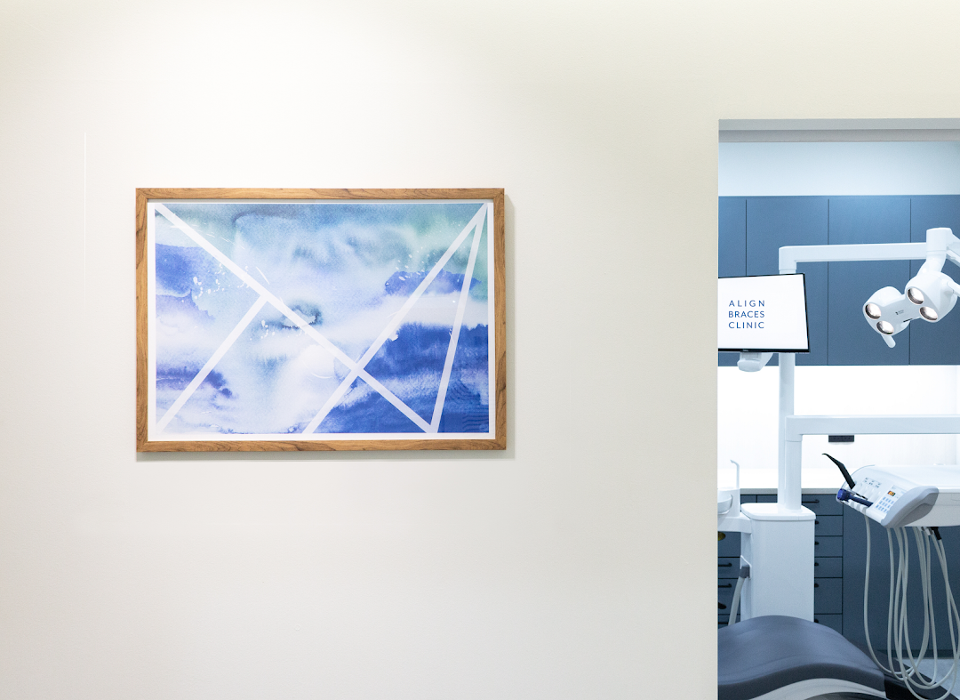 A modern dental clinic interior featuring a treatment chair, equipment, and wall art.