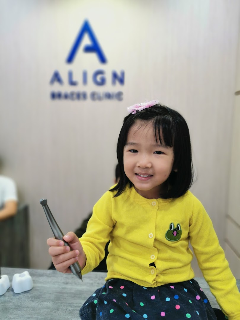 A smiling child holds a dental tool inside Align Braces Clinic.