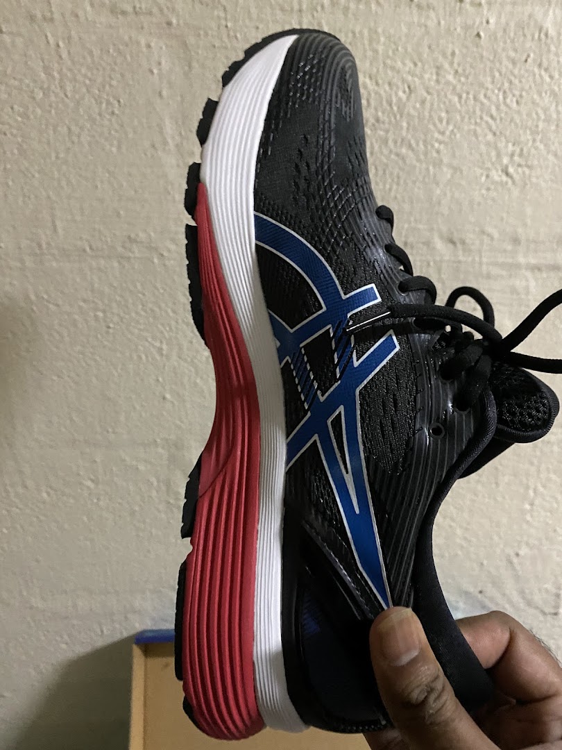 A hand holding a black ASICS running shoe with blue and red accents.