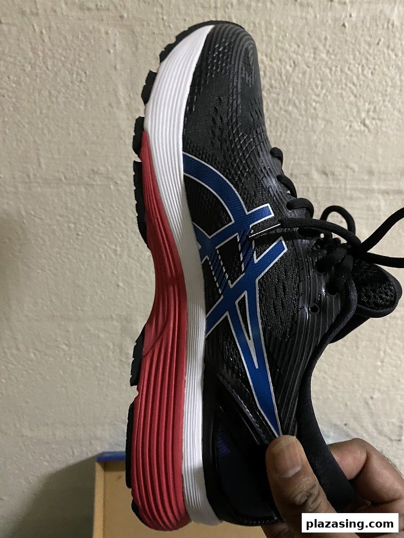 A hand holding a black ASICS running shoe with blue and red accents.