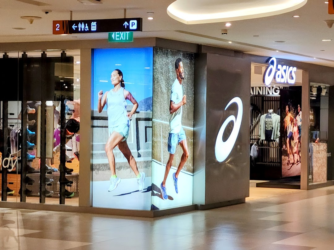 The ASICS shop entrance features large digital displays showcasing runners and athletic wear in a mall.