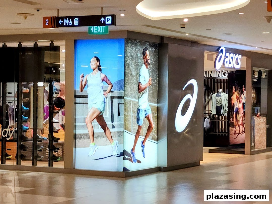 The ASICS shop entrance features large digital displays showcasing runners and athletic wear in a mall.