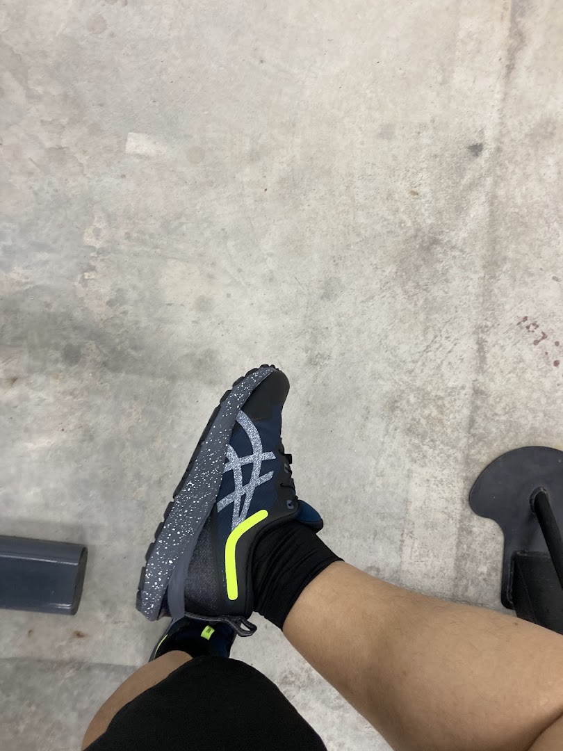 A person's leg wearing a dark blue ASICS running shoe with a speckled sole and yellow accent.