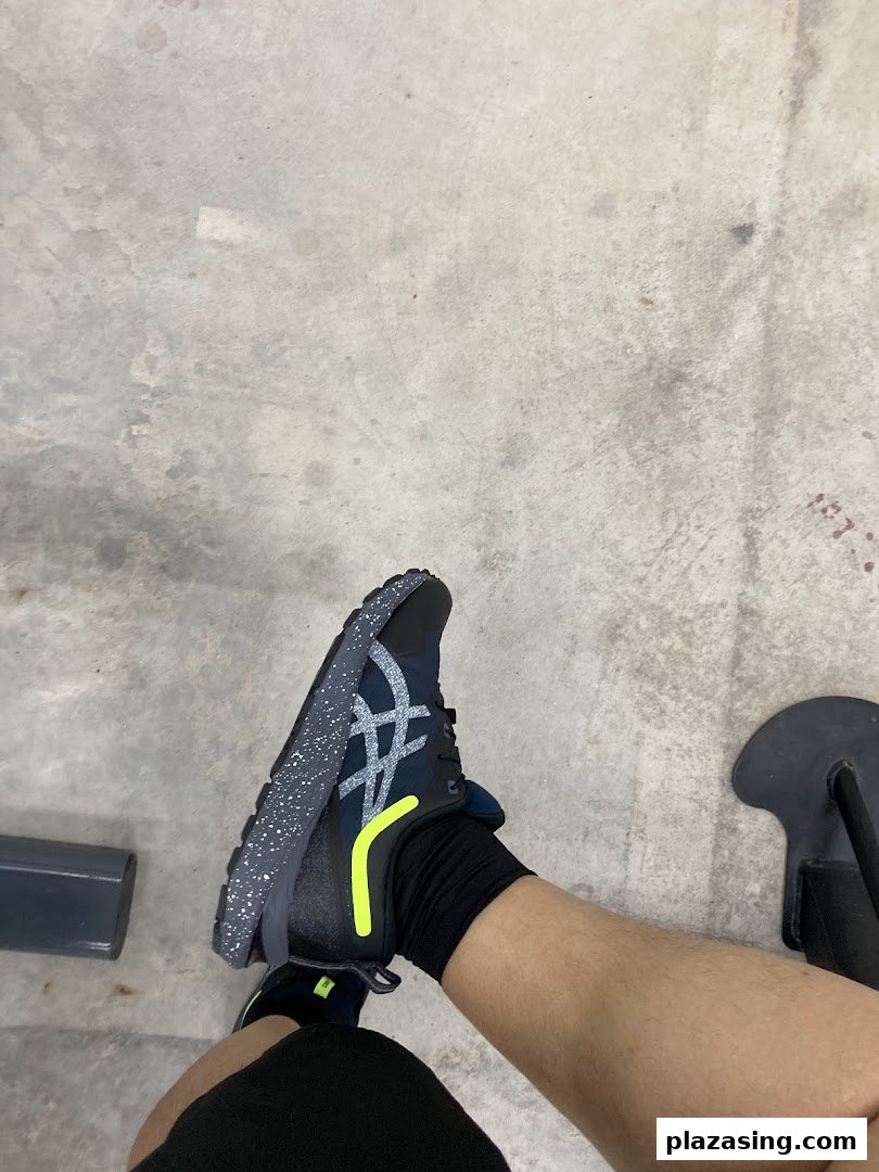 A person's leg wearing a dark blue ASICS running shoe with a speckled sole and yellow accent.