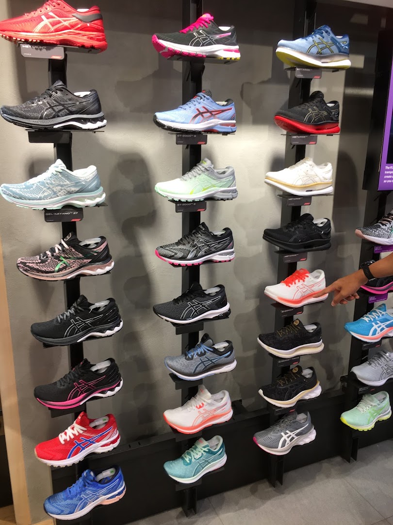 A wall display showcasing a wide variety of colorful ASICS running shoes in a retail store.