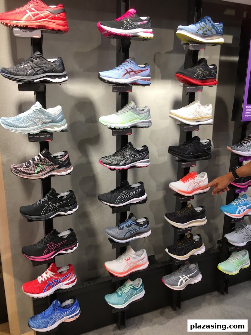 A wall display showcasing a wide variety of colorful ASICS running shoes in a retail store.