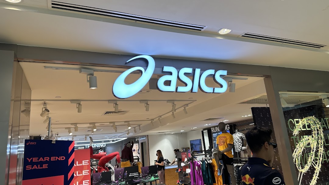 The brightly lit entrance of an ASICS retail store, showcasing its prominent logo and inviting interior.