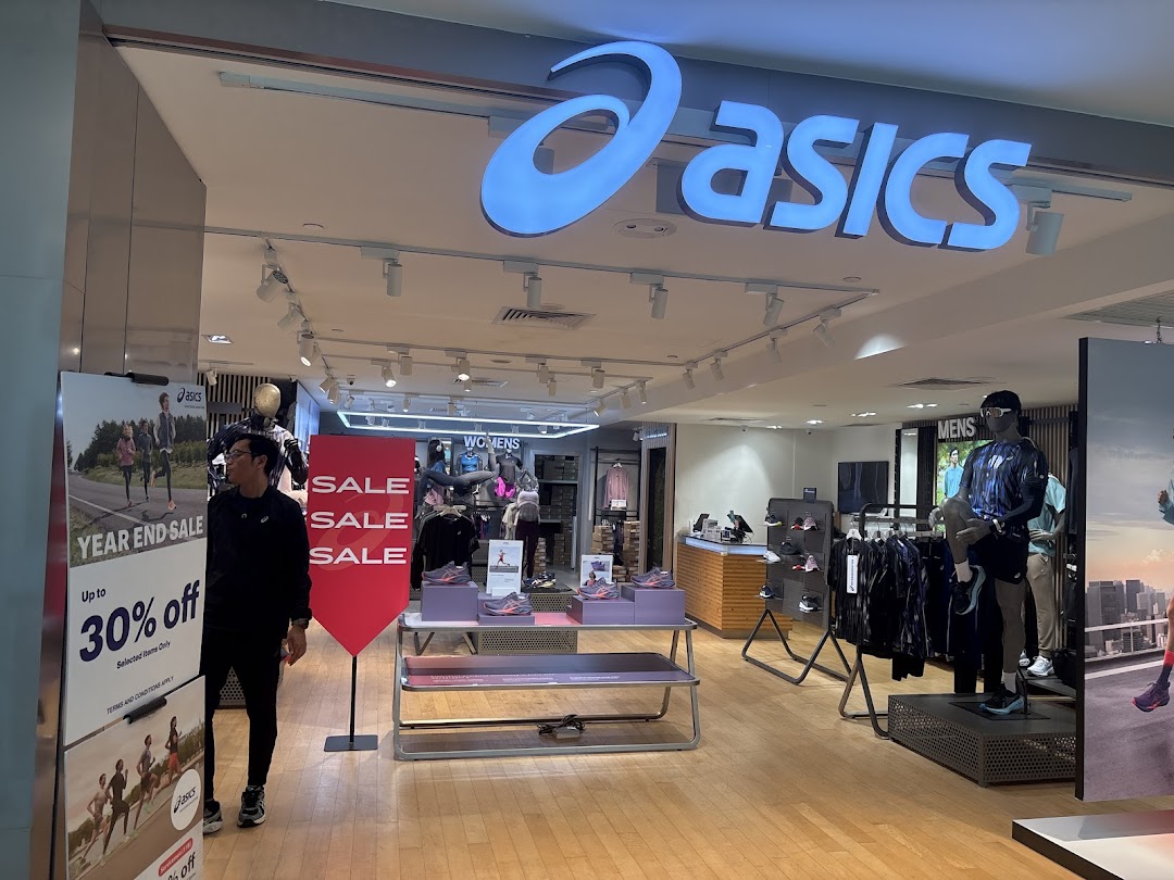 The ASICS store entrance features its prominent logo, sale signage, and athletic apparel displays.
