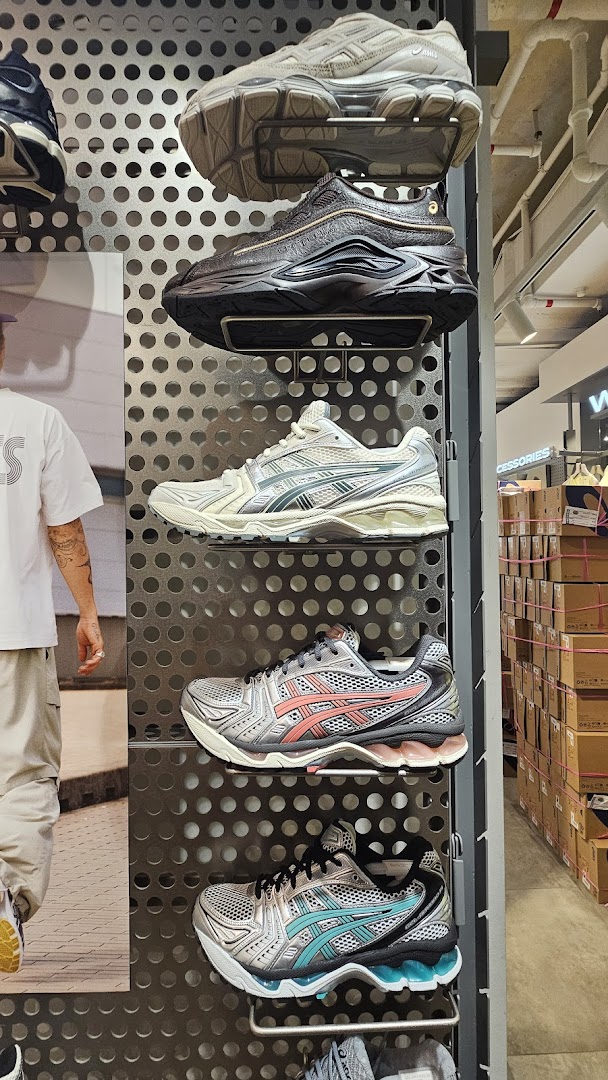 A display of various ASICS sneakers on a perforated wall rack inside the store.