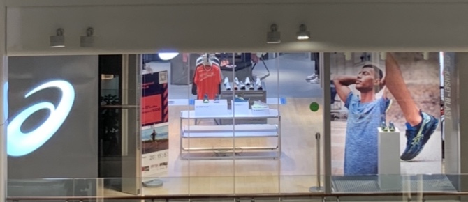 The ASICS shop front features athletic footwear, apparel, and large promotional displays.