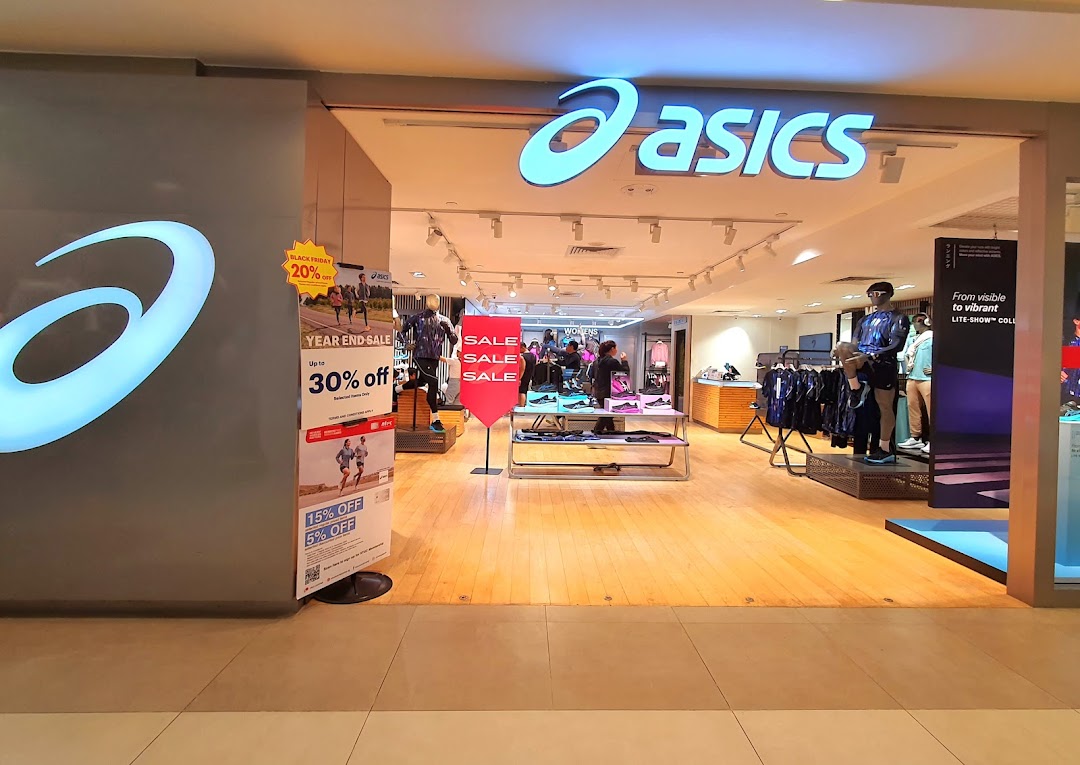 The brightly lit entrance of an ASICS store showcasing athletic footwear, apparel, and sale promotions.