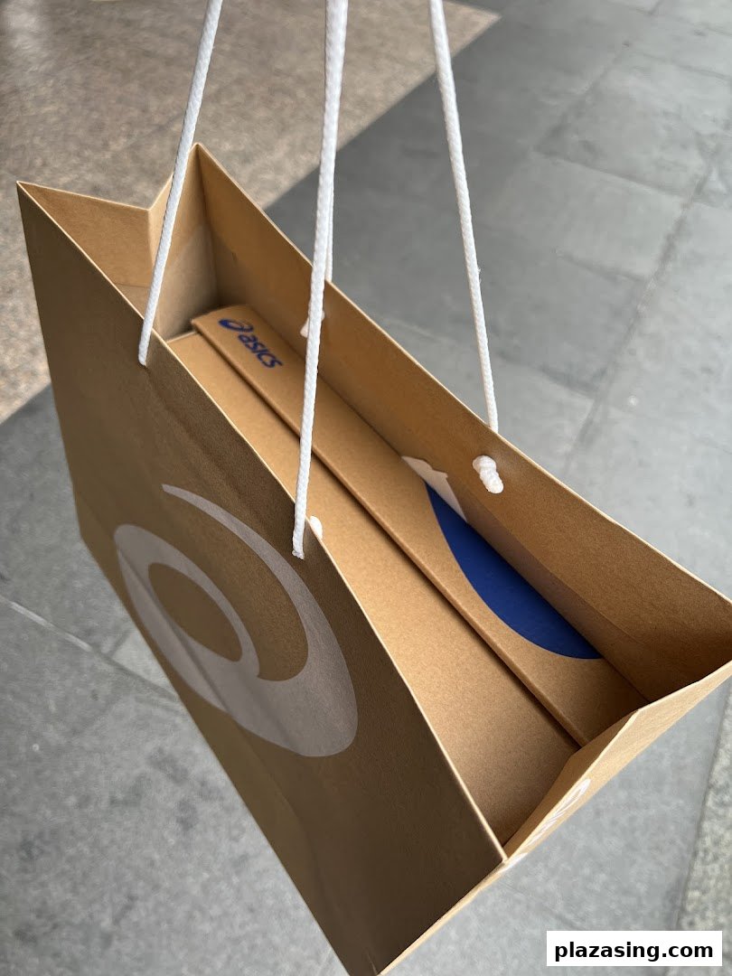 A brown ASICS shopping bag with white handles and logo, containing a product box.